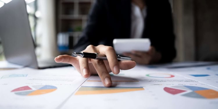 A person's hand holding a pen and pointing down at a printed graph at a desk.