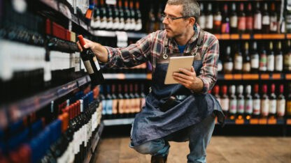 Salesman with digital tablet taking stock of wine