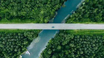 Overhead photo of blue vehicle crossing highway over river in forest.